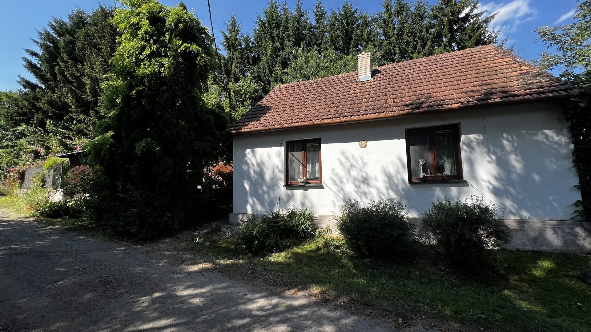 Bílý rodinný dům s taškovou střechou obklopený vzrostlými stromy, poslední dům v klidné ulici v Krokocíně